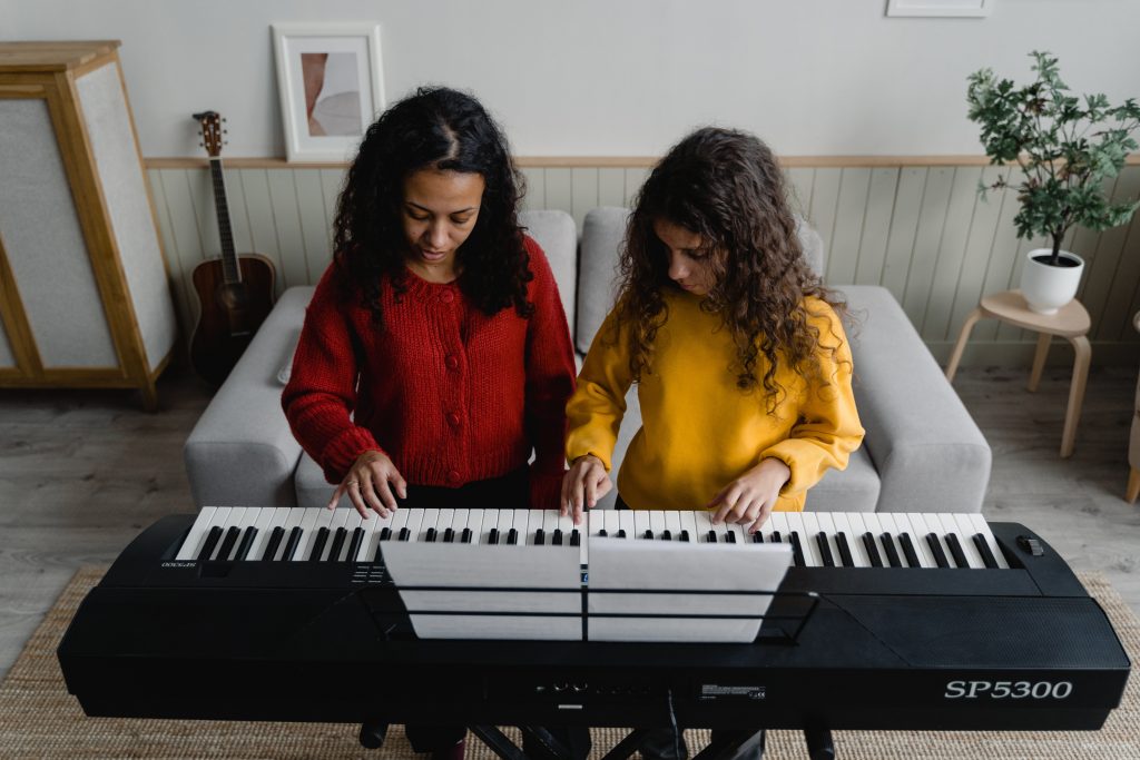 activités extra scolaires : une jeune fille apprend à jouer du piano avec sa professeur
